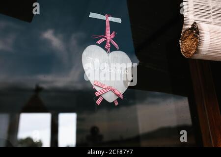 Esterno di una vecchia finestra in legno decorata con tende bianche e il cuore di carta fissato al vetro Foto Stock