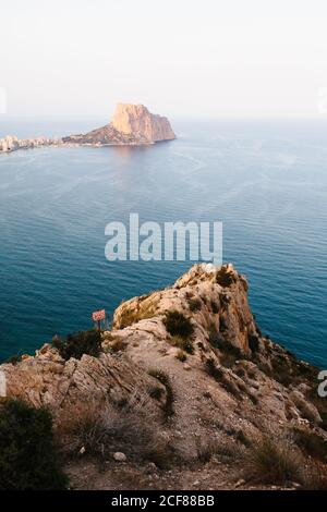 Vista ad alto angolo del mare calmo che si increspa vicino a ruvidi rocce riva con scogliera sassosa che si erge sull'acqua in lontananza Foto Stock