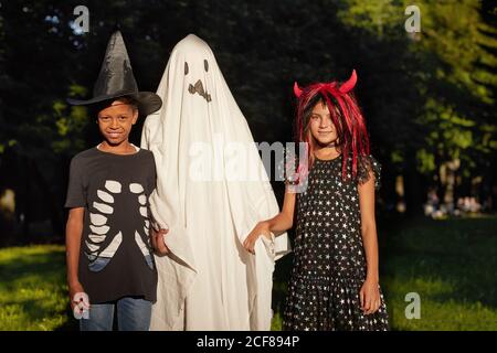 Ritratto di bambini in costumi di strega e fantasma sorridente Con la fotocamera durante la festa all'aperto di Halloween Foto Stock