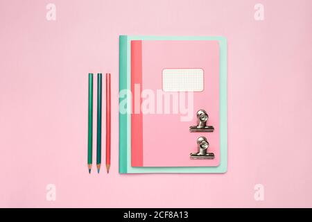 Da sopra composizione di taccuini colorati, penna, matite, righello e graffette disposte su scrivania rosa Foto Stock