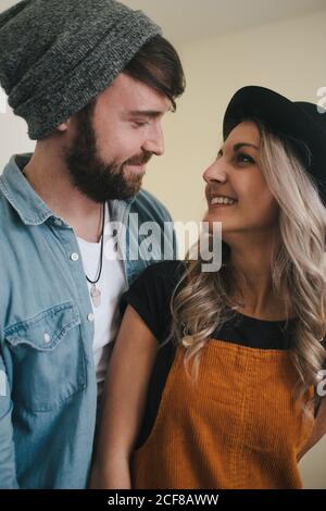 Donna allegra in cappello e ragazzo sorridente in giacca denim coccole mentre in piedi in cucina guardando l'un l'altro Foto Stock
