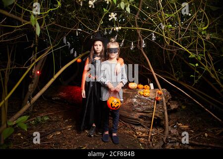 Ritratto di due bambini in costumi di Halloween guardando la macchina fotografica mentre si è in piedi nella preda oscura Foto Stock