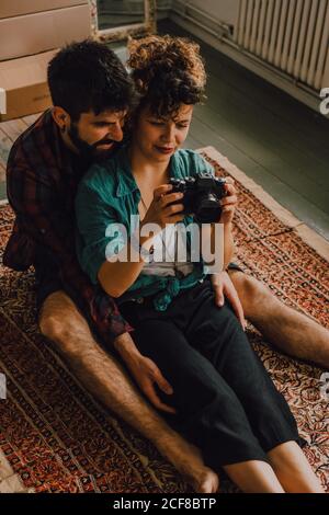 Dall'alto la vista dell'uomo e della donna hipster che usano la macchina fotografica che siede a piedi nudi sul pavimento dell'appartamento Foto Stock