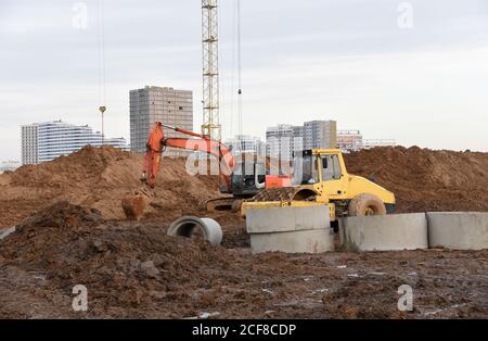 Vibrazione del rullo per la circolazione su strada monocilindrico e dell'escavatore in cantiere. Attrezzature pesanti per lavori su strada e a terra. Scavo fondazione e posa su Foto Stock