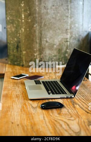 Netbook moderno collocato su un tavolo di legno con smartphone e mouse in un'accogliente caffetteria Foto Stock