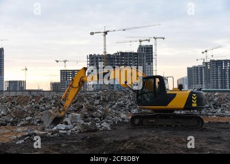 Escavatore giallo in un cantiere durante la frantumazione di pietre dopo la demolizione di un vecchio edificio. Recupero e riciclaggio dei rifiuti di costruzione. Re Foto Stock