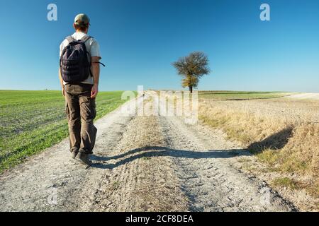 Uno zaino in spalla su una strada sterrata va in una giornata di sole. Foto Stock