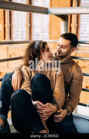 Allegro giovane uomo e donna abbracciarsi e guardarsi mentre si siede all'interno del padiglione illuminato durante la data Foto Stock