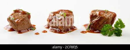 Tre singoli cubetti di goulash di manzo in salsa cosparsi di prezzemolo fresco tritato isolato su bianco in un banner panoramico Foto Stock