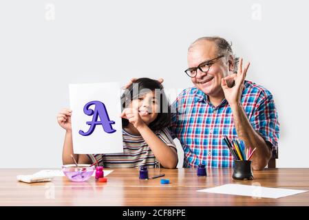 Buon nonno indiano e piccola nipote pittura con pennello e colori dell'acqua. Bambini art. Tempo libero con il nipote Foto Stock