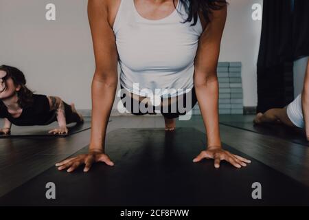 Crop Unriconoscable fit barefooted femmina in sportswear messa a fuoco e fare una tavola con zampe posa sul tappeto sportivo mentre allenati con altri atleti al piano in una spaziosa palestra moderna Foto Stock