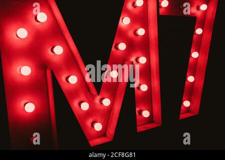 Lettera M enorme con lampade al neon rosso illuminanti su nero muro al buio Foto Stock