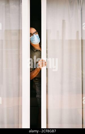 Donna adulta in maschera medica guardando fuori sulla strada con Paura durante la pandemia di COVID 19 Foto Stock