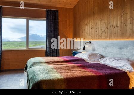 Due letti comodi e puliti con cuscini bianchi e caldi e colorati coperte in camera luminosa e accogliente con pareti gialle contro la finestra con tende blu che si affacciano sul paesaggio rurale Foto Stock