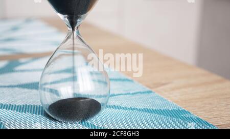 Closeup di clessidra su un tavolo di legno bianco con cucina sfocata su sfondo. Concetto di tempo per cucinare. Foto Stock