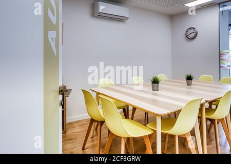 Interni dal design moderno di un ufficio luminoso e spazioso, con zone in vetro parete con comode sedie gialle e sgabelli grigi tavoli in legno Foto Stock