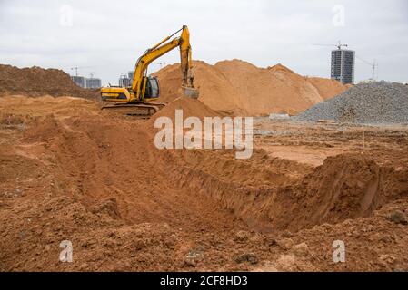 Escavatore a terra in cantiere. Il caricatore di retroescavatore scava una buca per la costruzione della fondazione. Scavo per la posa di tubi fognari Foto Stock