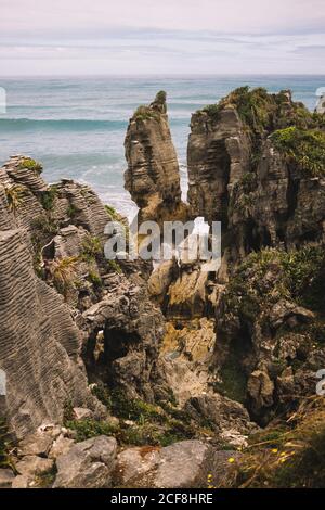 Dall'alto di rocce sovrastate di piante conchite di onde E cielo nuvoloso in Pancake Rocks in Nuova Zelanda Foto Stock