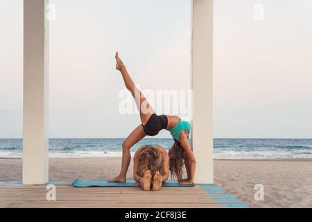 Flessibile Donna fare ponte in acroyoga sullo sfondo dell'oceano Foto Stock