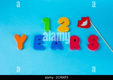 12 anni festeggiando il logo classico.cute Masquerade maschere labbra su bastone. Colorato felice anniversario 12 ° numeri su sfondo blu. Saluti celebra card.cifre tradizionali di età. Disposizione piatta. Foto Stock