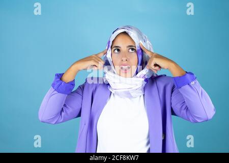Giovane bella donna araba che indossa hijab islamico su sfondo blu isolato sorridendo e pensando con le dita sulla testa che ha un'idea. Foto Stock