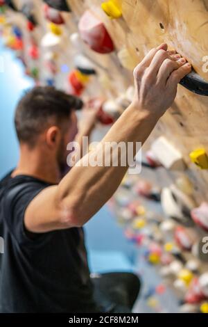 Vista dall'alto laterale dell'atleta maschile in abbigliamento sportivo con le mani in talco polvere che tiene sulle impugnature addestramento dentro palestra Foto Stock