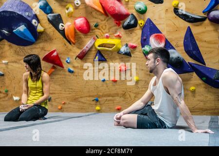Vista laterale di un uomo e una donna sorridenti e muscolosi seduti sul pavimento e sorridenti mentre si allenano in palestra Foto Stock