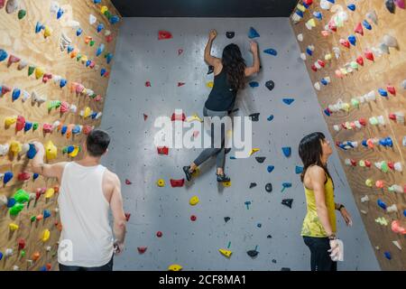 Vista laterale di scalatori professionisti di sesso maschile e femminile in attivo indossare appeso alla parete e leggere l'alpinismo d'abeti in moderno palestra Foto Stock