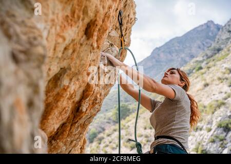 Impavida giovane alpinista femminile ascendente su scogliera verticale in montagna luogo in estate Foto Stock