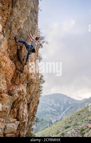Impavida giovane alpinista femminile ascendente su scogliera verticale in montagna luogo in estate Foto Stock