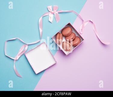 macaron rotondi multicolore cotti in scatole quadrate su sfondo pastello colorato, vista dall'alto Foto Stock