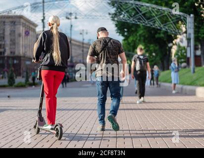 Irriconoscibile giovane donna che guida scooter elettrico a spinta sulla strada della città. Vista posteriore. Concetto di trasporto alternativo eco-compatibile in città Foto Stock