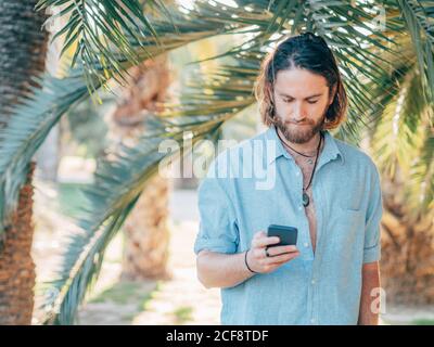 Giovane uomo hipster con bearded che indossa una maglietta blu sul telefono nella giungla tropicale Foto Stock