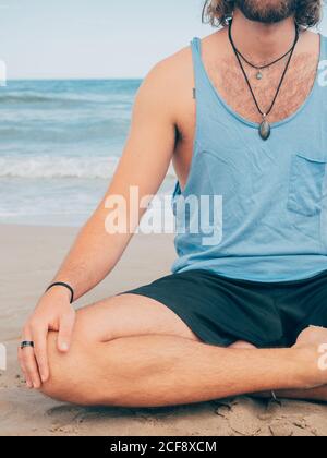 Crop irriconoscibile sportivo bearded maschile formazione su tranquilla mare e. fare yoga asana contro mare blu e cielo Foto Stock