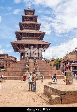 NEPAL, KATHMANDU - 4 AGOSTO 2014: Strada con le persone e gli edifici vicino a splendida torre alta con gradini e cielo blu Foto Stock