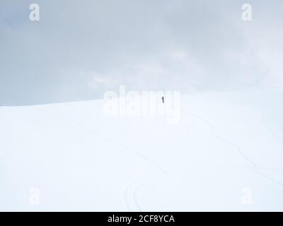 Figura scura di persona sola che cammina su una collina innevata dentro giorno nuvoloso Foto Stock