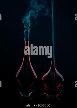Due bottiglie di vetro fragili che emettono fili di fumi sottili sfondo nero Foto Stock