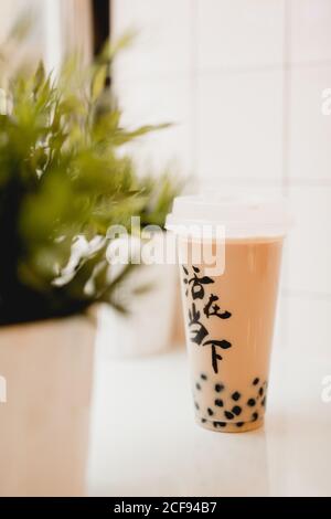 Gustoso tè con bolle di latte con perle di tapioca in tazza di plastica Sul tavolo vicino a piante in vaso nel tradizionale cafe' di Taiwan Foto Stock