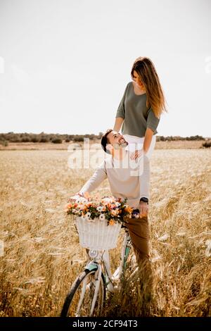 Uomo e donna seducente in bicicletta decorata alla luce del sole sul campo di segale dorato in estate Foto Stock