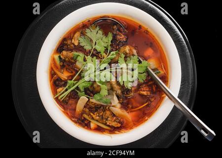 Da sopra gustosa zuppa di rana calda con carne di rana, cipolla, cetriolo e coriandolo su piatto su fondo nero Foto Stock