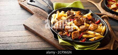 Delizioso gulasch di cervo selvatico tedesco con peperoncino rosso caldo E patatine fritte servite in una padella rustica a taverna in un banner panorama con copysp Foto Stock