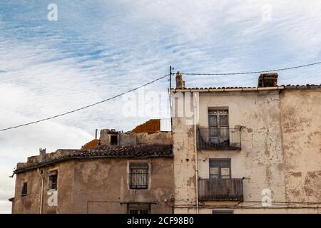 Basso angolo di antiche case residenziali in pietra rovinata con shabby pareti e balconi situati nel quartiere della città contro il cielo nuvoloso Foto Stock