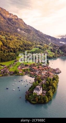 Da sopra drone vista della piccola penisola con vecchio Iseltwald castello e villaggio situato sulla riva del lago in montagna Terreno in Svizzera al tramonto in estate sera Foto Stock