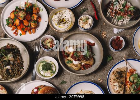 Dall'alto di vari piatti orientali e spuntini organizzati con salse e posate su superficie grigia Foto Stock