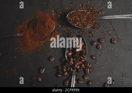 Tipi di caffè macinato istantaneo e in polvere e in chicchi di caffè in cucchiai su tavola nera Foto Stock