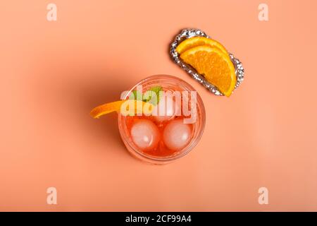 Vista dall'alto del cocktail alcolico con cubetti di ghiaccio e sprig di menta in vetro posto su sfondo rosa con arancio sezioni Foto Stock
