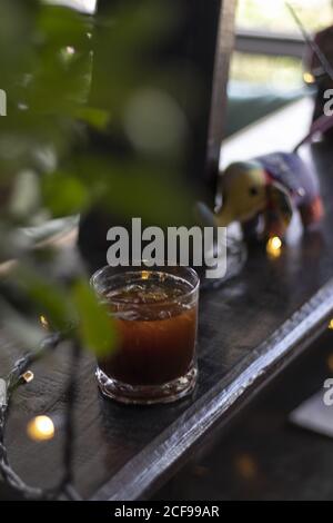 Immagine verticale ad alto angolo di un bicchiere di nero ghiacciato caffè su un tavolo da caffè con luci Foto Stock