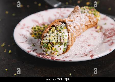 Cannoli siciliani fatti in casa con ricotta ripieno guarnito con pistacchi e. zucchero in polvere e posto su tavolo di legno in cucina Foto Stock
