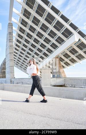 Vista laterale della giovane donna che guarda la macchina fotografica mentre balla su un alto e contemporaneo edificio in cemento Foto Stock