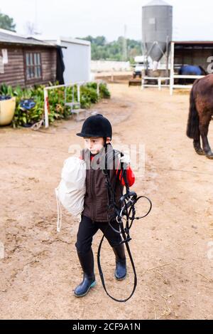 Piccolo fantino che trasporta l'attrezzatura sull'arena dopo l'addestramento in equestre scuola Foto Stock